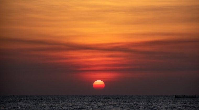 黄昏时分临海的巨大礁石群伸向海面，远处海天线与晚霞相接，画面呈现海角天涯般的辽远孤寂氛围